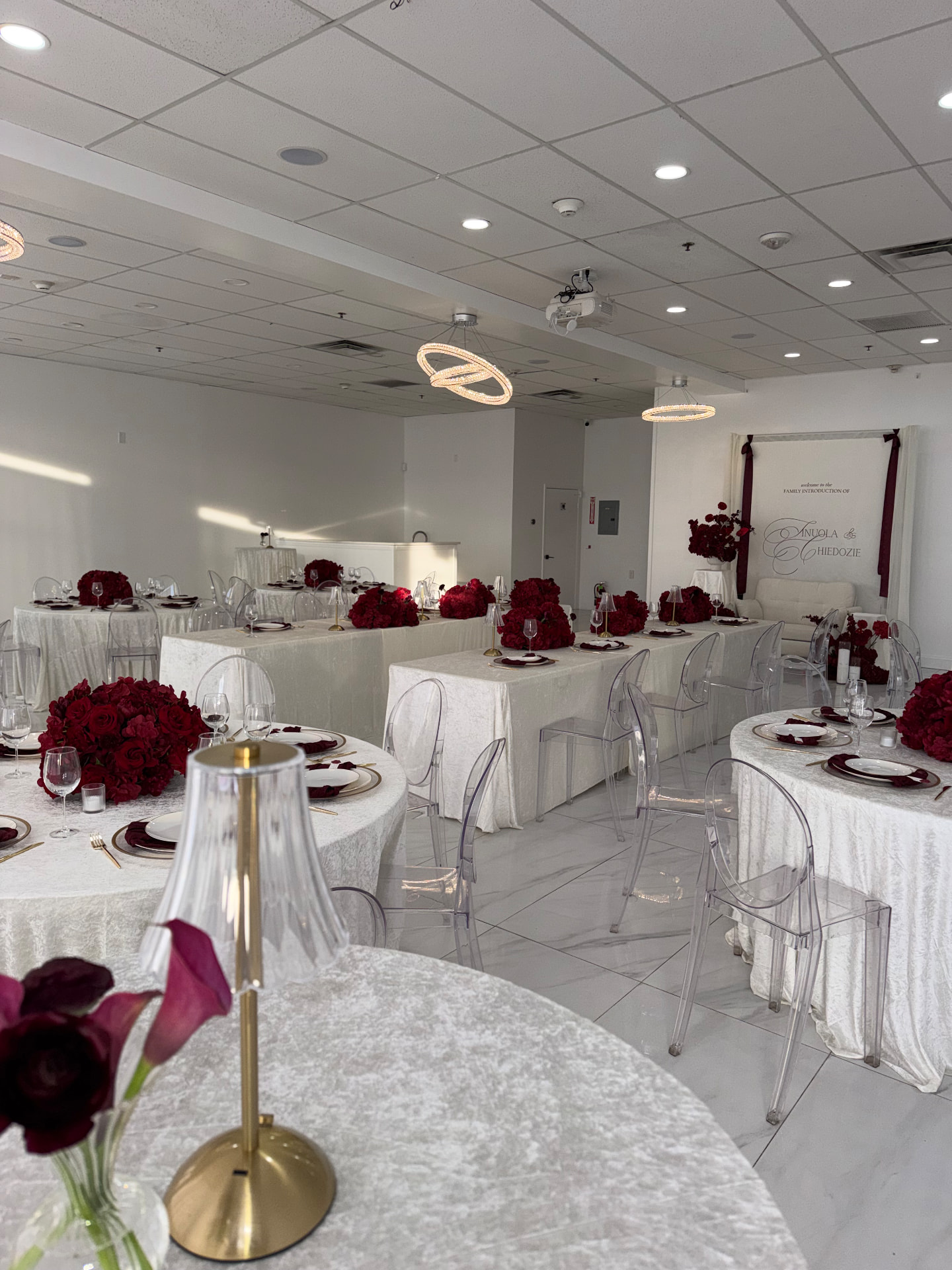 Reception room with crimson rose centerpieces, ivory velvet linens and ghost chairs