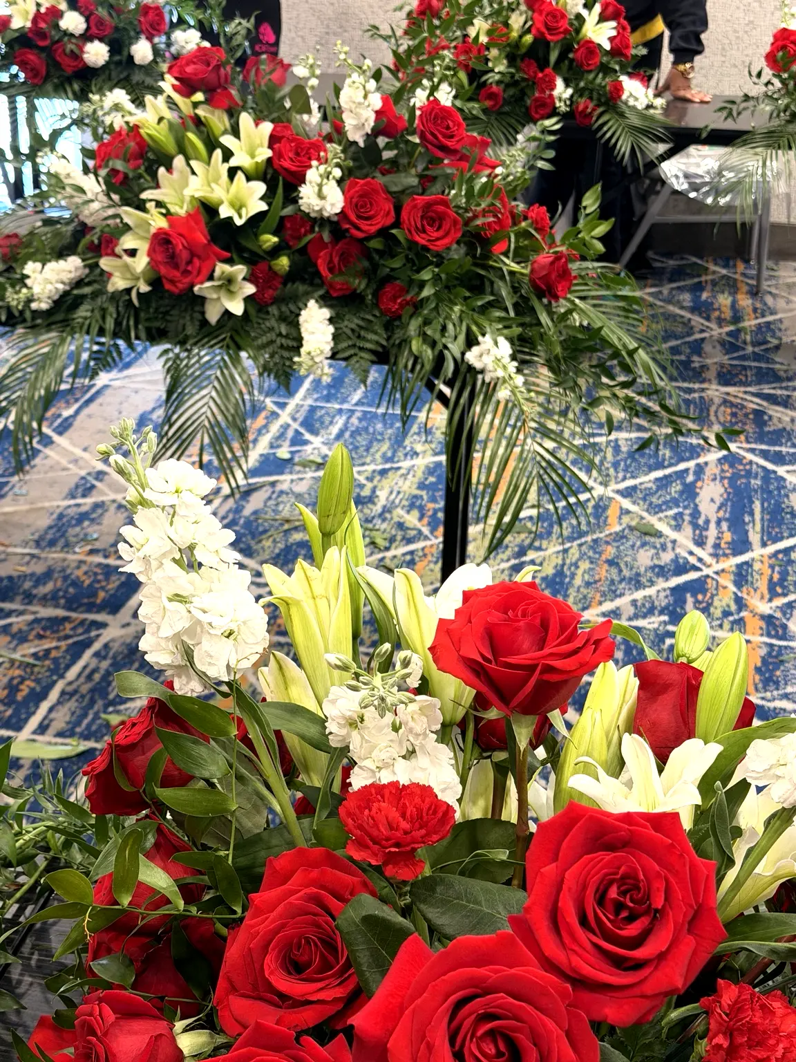 Casket arrangement of red roses, white lilies and stock with greenery at a service